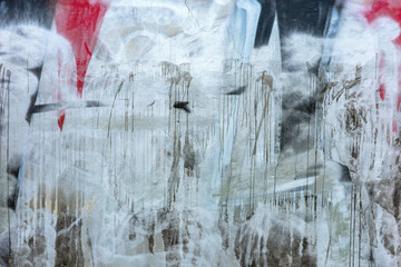 This urban surface presents a weathered concrete wall heavily layered with expressive, drippy graffiti in shades of silver, black, and red.