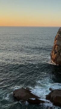 Distinctive sea stack standing in the Atlantic Ocean in warm sunset light, with gentle camera movement, calm waves and natural sea sound along the rocky coastline of Costa Quebrada, Cantabria, Spain.