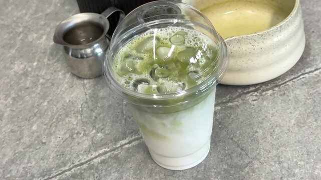 poor quality matcha is swamp green Iced matcha latte preparation in clear plastic cup showing pale green color uneven texture and diluted tea drink served with ice and black straw