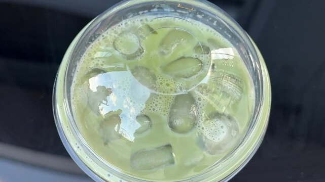 poor quality matcha is swamp green Iced matcha latte preparation in clear plastic cup showing pale green color uneven texture and diluted tea drink served with ice and black straw