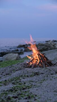 Bonfire burning on a rocky beach at dusk with sound of ocean waves