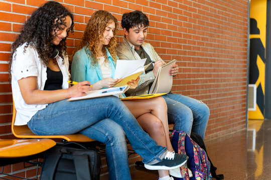 University students sitting, studying, and working together on campus hallway