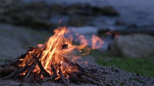 Bonfire burning on a rocky beach at dusk with sound of ocean waves