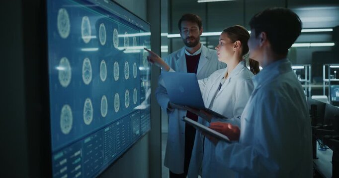 Diverse Team of Medical Scientists Talk in Meeting, Discussing MRI Brain Scans on Interactive Display and Laptop in Modern Research Hospital Laboratory, Collaborating on Neurology Drug Development