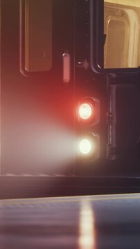 A train approaches the station as evening falls. Lights shine brightly from the front of the train. The platform is quiet with few people present.