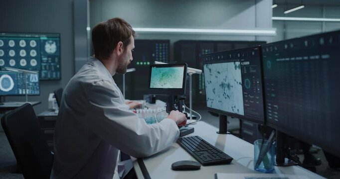  Male Medical Scientist Uses Digital Microscope to Analyze Cell Samples on Screen, Referencing MRI Brain Scans While Colleagues Work on Drug Development for Disease Treatment in Hospital Laboratory