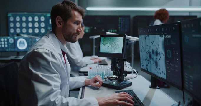 Scientist Uses Digital Microscope to Analyze Molecular Samples and Reviews MRI Brain Scans on Monitors in Hospital Laboratory While Female Researchers Develop Disease Treatments. Zoom out shot