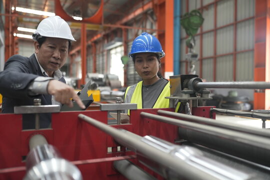 Factory workers discuss project details inside a manufacturing facility while observing machinery in operation