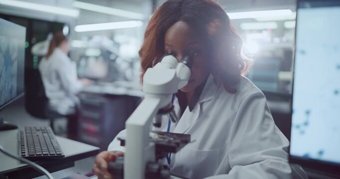 Portrait of Focused African American Female Scientist Using Digital Microscope to Analyze Samples in Medical Research Hospital, Colleagues Developing Drugs for Disease Treatment. Slow Motion