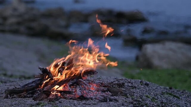 Bonfire burning on a rocky beach at dusk with sound of ocean waves