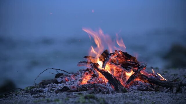 Bonfire burning on a rocky beach at dusk with sound of ocean waves