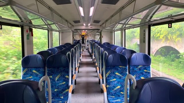 Train interior with blue seats moving through scenic green landscape in Germany. Regional train passing stone arch bridges and green trees visible through large windows. 4K footage
