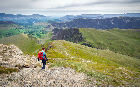 A female hiker descending the ridge of High Snab Bank, ridgeline, from the summit of Robinson with Newlands in the distance in the English Lake District, UK.