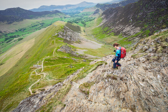 A female hiker descending the rocky ridge of High Snab Bank, ridgeline, from the summit of Robinson with Newlands in the distance in the English Lake District, UK.