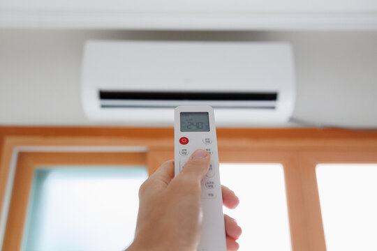 Close up of a hand using a remote control to operate a wall mounted air conditioner. Indoor climate control. Home cooling system. Energy efficient air conditioning. Smart home technology.