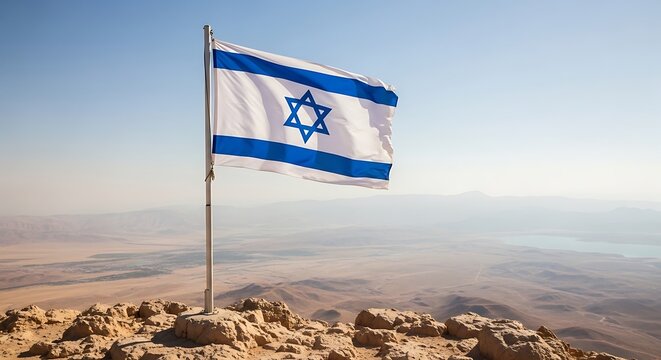 National flag of Israel waving on a tall pole on top of a rocky mountain under a bright blue sky with soft clouds