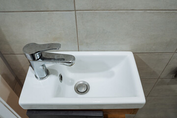 Fototapeta premium Compact white ceramic sink with chrome faucet against tiled wall