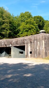 A wide, panning outdoor view of the massive concrete entrance block at Fort de Schoenenbourg, a major historical fortification along the legendary French Maginot Line. Shot in vivid color.