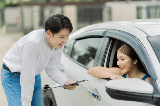 A beaming young woman sits in her new car while talking to a car dealer, reflecting a car-related lifestyle.