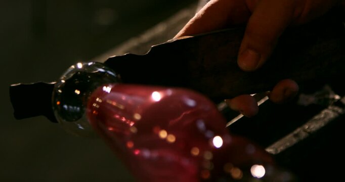 Close up of a hand holding a blowpipe with a glowing red piece of molten glass being shaped
