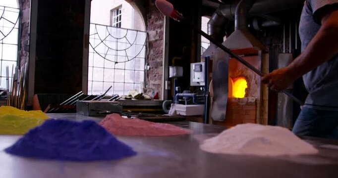 Glass blower using a blowpipe to gather molten glass from a furnace in a workshop