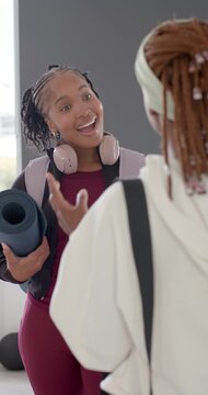 Vertical video: African American women entering studio in burgundy with mat greeting planning class