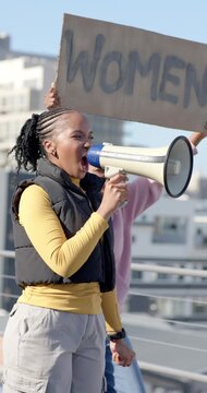 Vertical video: Adult woman leading protest, marching overpass, shouting into megaphone, sign WOMEN