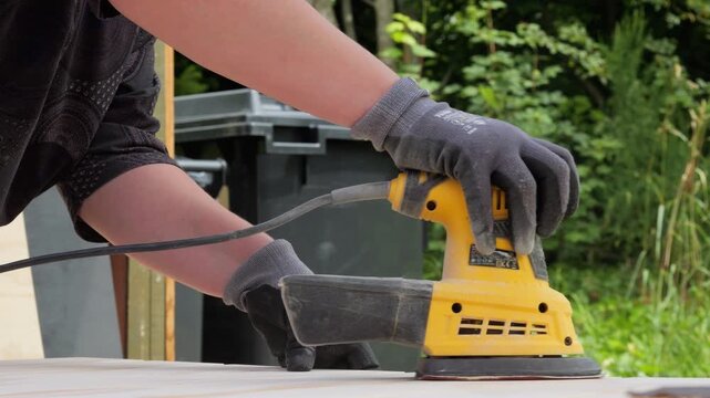 Carpenter sanding wood with an electric sander