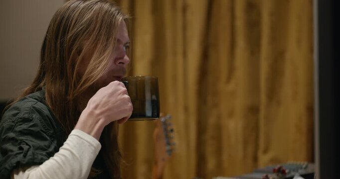 Caucasian man drink hot water in home sound recording studio while working. Single male is drinking tea in evening. 4K 10-bit