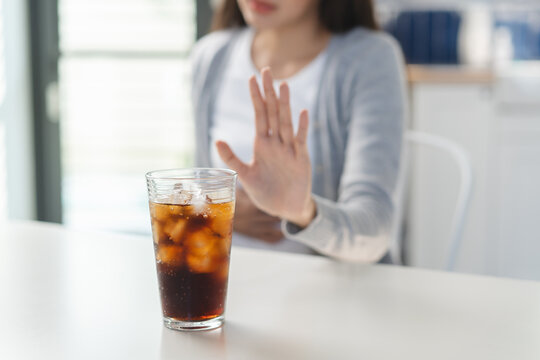 Close up of a young woman making a stop gesture to refuse a glass of cola or soft drink.