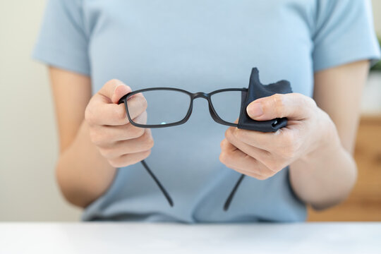 Close-up person cleaning eyeglasses with microfiber fabric.