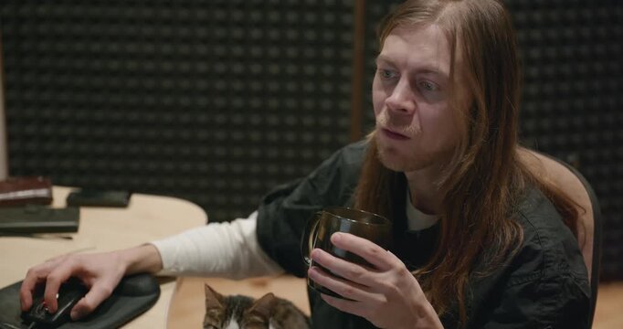 Caucasian man drink hot water in home sound recording studio while working. Single male is drinking tea in evening. 4K 10-bit