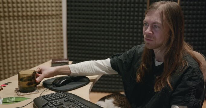 Caucasian man drink hot water in home sound recording studio while working. Single male is drinking tea in evening. 4K 10-bit