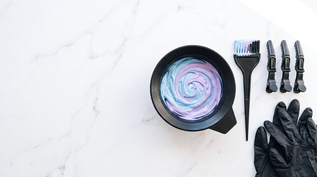 Mixing pastel hair color in a salon bowl with professional tools on a white marble background