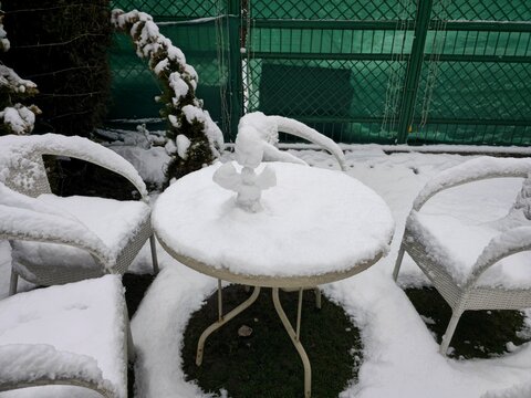 Beautiful winter morning scene in Manali showing outdoor garden patio furniture, including white chairs and a round table, heavily coated in fresh snow.