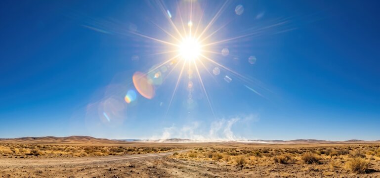 Blazing sun with lens flare over a dry, arid desert landscape with a dirt road and sparse vegetation