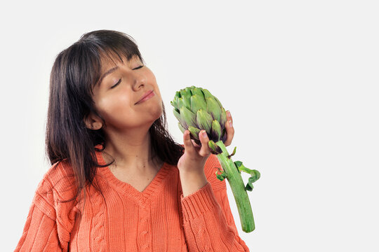 Woman smells fresh artichoke with closed eyes
