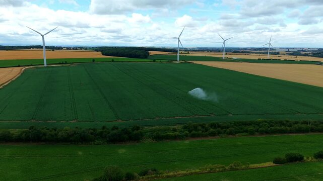 Aerial view of farm crops being irrigated with a jet pump, wind turbines in the background during summer drought, UK.