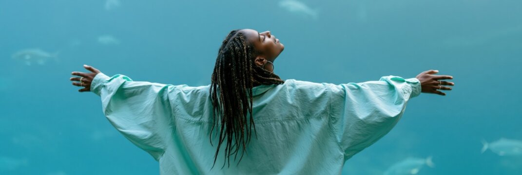 Woman with open arms inside large aquarium with swimming fish for serene marine background banner and website hero image