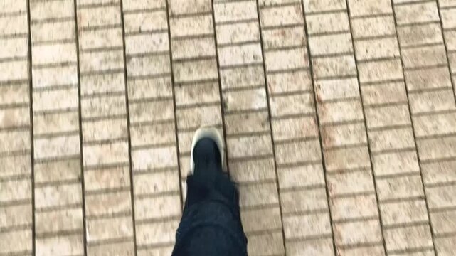 POV first person view of walking on wet pavement with textured tiles. Female feet in jeans and sneakers step across a tiled surface in a top down perspective. Concept of point of view,