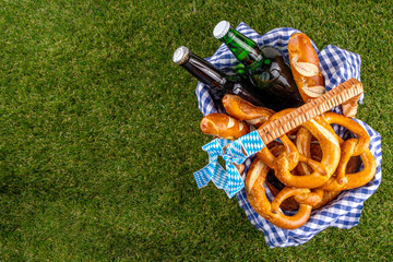 Fototapeta premium Oktoberfest picnic and barbecue food, bavarian party menu, bavarian sausages, pretzels, potato, sauerkraut, beer bottles, with picnic basket, checkered napkin tablecloth, Oktoberfest festive ribbon