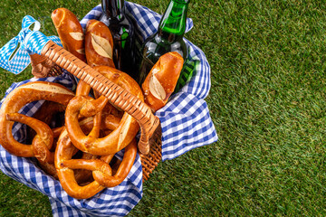 Fototapeta premium Oktoberfest picnic and barbecue food, bavarian party menu, bavarian sausages, pretzels, potato, sauerkraut, beer bottles, with picnic basket, checkered napkin tablecloth, Oktoberfest festive ribbon