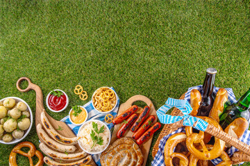 Fototapeta premium Oktoberfest picnic and barbecue food, bavarian party menu, bavarian sausages, pretzels, potato, sauerkraut, beer bottles, with picnic basket, checkered napkin tablecloth, Oktoberfest festive ribbon