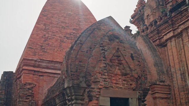 Nha Trang Vietnam. 01 06 2026 Ancient red brick temple entrance with carved arch, towering chedi, weathered masonry, trimmed shrubs, and tall chedi rising behind under soft overcast light in Vietnam