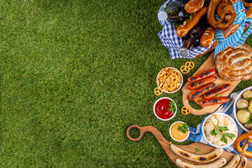 Fototapeta premium Oktoberfest picnic and barbecue food, bavarian party menu, bavarian sausages, pretzels, potato, sauerkraut, beer bottles, with picnic basket, checkered napkin tablecloth, Oktoberfest festive ribbon