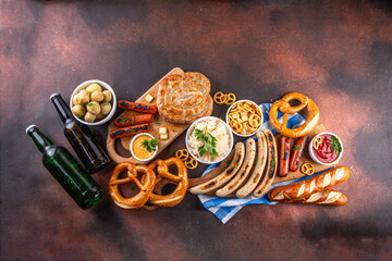Fototapeta premium Oktoberfest picnic and barbecue food, bavarian party menu, bavarian sausages, pretzels, potato, sauerkraut, beer bottles, with picnic basket, checkered napkin tablecloth, Oktoberfest festive ribbon