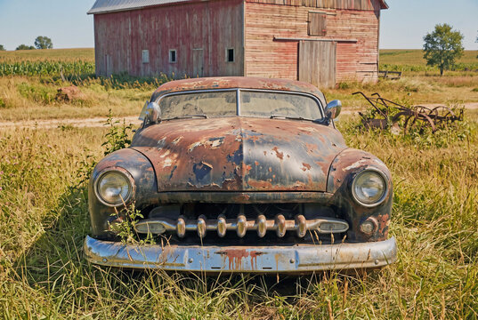 antique automobile rusting in a field near a country barn