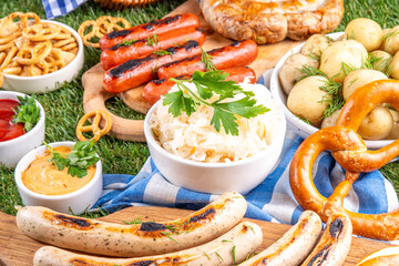 Fototapeta premium Oktoberfest picnic and barbecue food, bavarian party menu, bavarian sausages, pretzels, potato, sauerkraut, beer bottles, with picnic basket, checkered napkin tablecloth, Oktoberfest festive ribbon