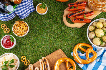 Fototapeta premium Oktoberfest picnic and barbecue food, bavarian party menu, bavarian sausages, pretzels, potato, sauerkraut, beer bottles, with picnic basket, checkered napkin tablecloth, Oktoberfest festive ribbon