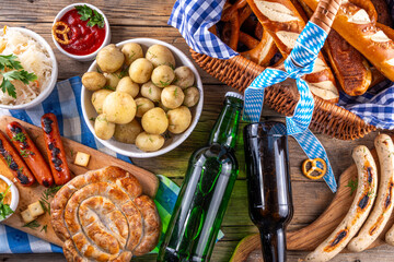 Fototapeta premium Oktoberfest picnic and barbecue food, bavarian party menu, bavarian sausages, pretzels, potato, sauerkraut, beer bottles, with picnic basket, checkered napkin tablecloth, Oktoberfest festive ribbon